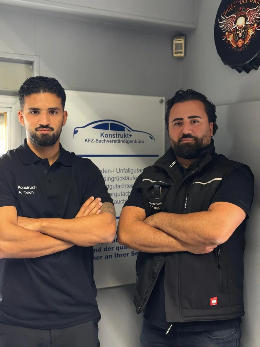 Amar Tekin (links) und Ing. Fatih Tekin (rechts) in schwarzer Arbeitskleidung mit Konstrukt+ Aufdruck, mit verschränkten Armen vor dem Firmenschild im Büro